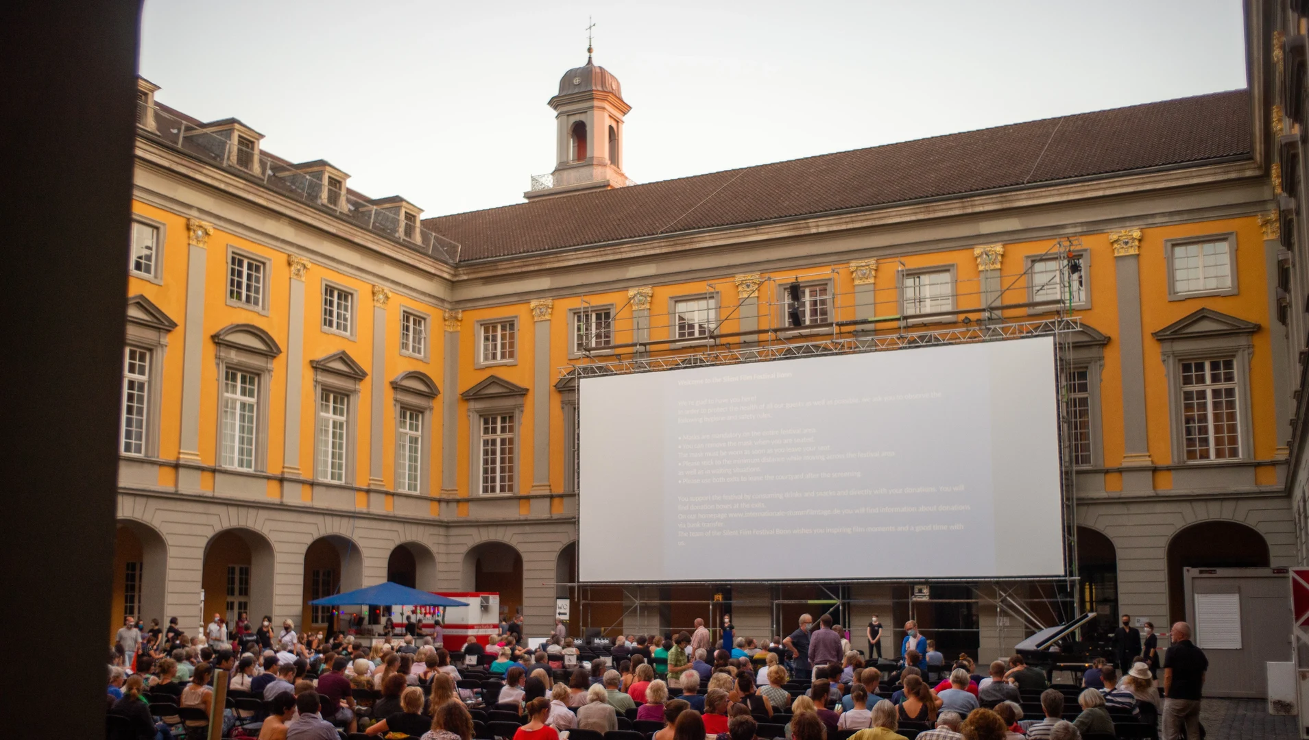 Eine Wissenschaftlerin und ein Wissenschaftler arbeiten hinter einer Glasfassade und mischen Chemikalien mit Großgeräten.